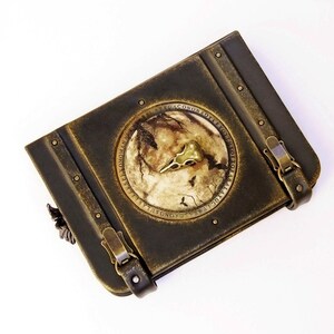 A vintage-looking book with a circular, raven scull embedded on the cover. The book features two metal clasps on its sides.