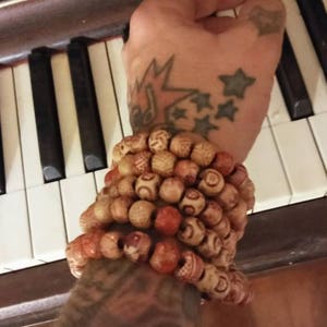 May include: A person's arm with a tattoo of stars and a lightning bolt wearing a stack of wooden bead bracelets. The bracelets are brown, red, and white.