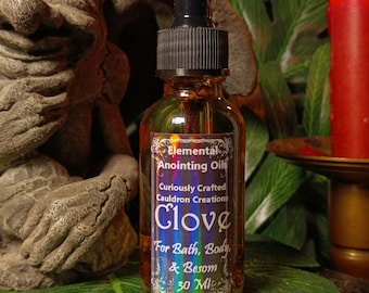 May include: A small glass bottle with a black dropper top and a label that reads "Elemental Anointing Oils Curiously Crafted Cauldron Creations Clove For Bath, Body & Besom 30 Ml".