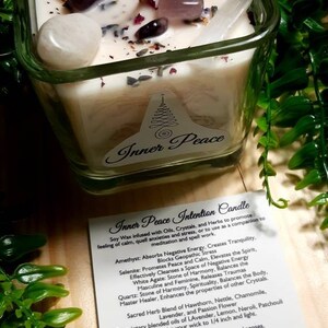 Pode incluir: Um frasco de vela quadrado de vidro com uma vela branca e v&aacute;rios cristais e ervas. A vela &eacute; etiquetada como "Inner Peace Intention Candle" e inclui uma descri&ccedil;&atilde;o dos cristais e ervas usados na vela. O texto inclui: Ametista, Selenita, &Aacute;gata branca, Quartzo, Espinho branco, Urtiga, Camomila, Lavanda, Flor da paix&atilde;o, Lim&atilde;o, Neroli, Patchouli. A vela est&aacute; sobre uma superf&iacute;cie de madeira com folhagem verde.