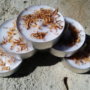 May include: A stack of six white tea light candles with a brown, flaky topping. The candles are arranged in a semi-circle.