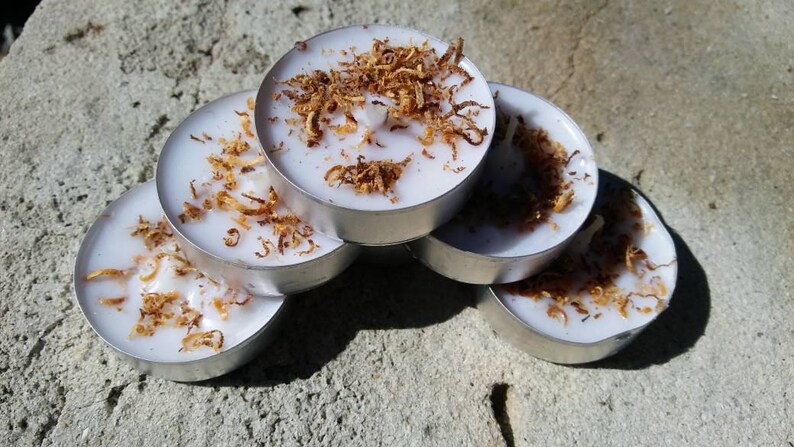 May include: A stack of six white tea light candles with a brown, flaky topping. The candles are arranged in a semi-circle.