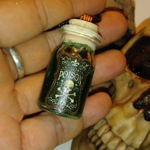 May include: A small glass bottle with a green liquid inside. The bottle has a cork stopper and a label that says "Poison" with a skull and crossbones.