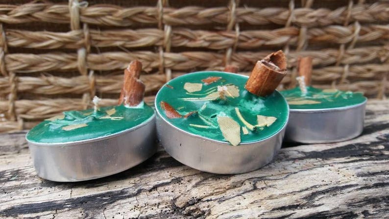 K&ouml;nnte beinhalten: Drei gr&uuml;ne Tee-Duftkerzen mit Zimtstangen darauf. Die Kerzen befinden sich in Metallbeh&auml;ltern und stehen auf einer Holzoberfl&auml;che.
