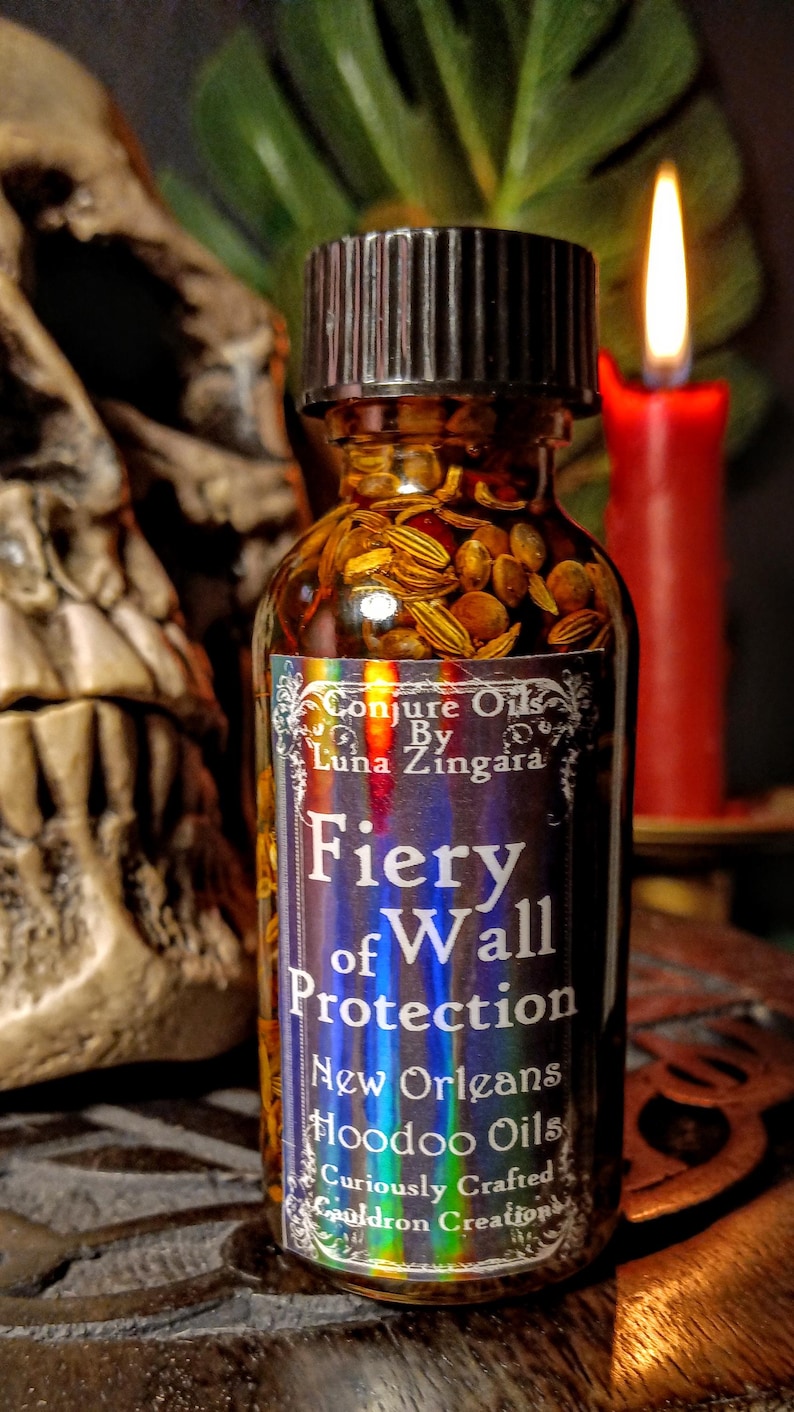 May include: A small glass bottle with a black cap filled with herbs and a label that reads "Conjure Oils By Luna Zingara Fiery of Wall Protection New Orleans Hoodoo Oils Curiously Crafted Cauldron Creations".