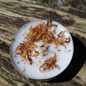 May include: A white tea light candle with a melted wax pool and brown wood shavings on top.