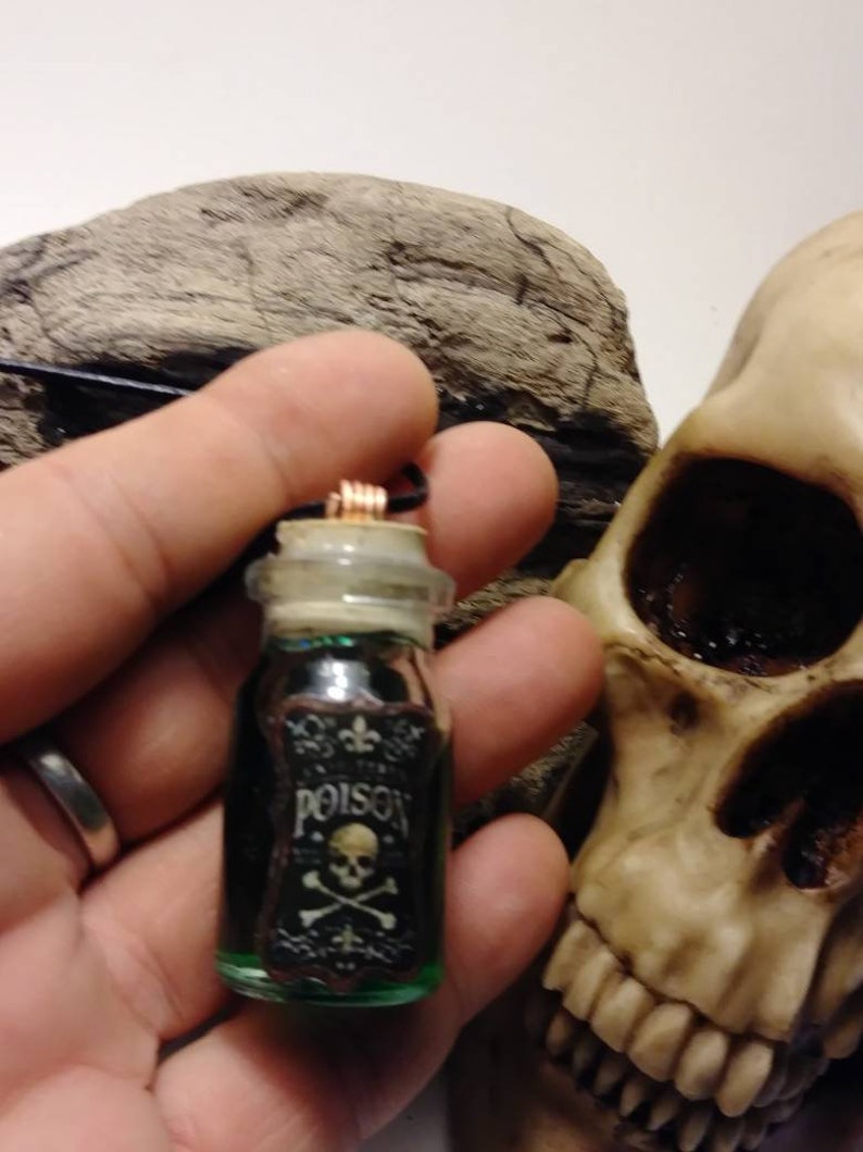May include: A small glass bottle with a cork stopper and a black label that reads "Poison" with a skull and crossbones. The bottle is filled with a green liquid and is hanging from a black cord.