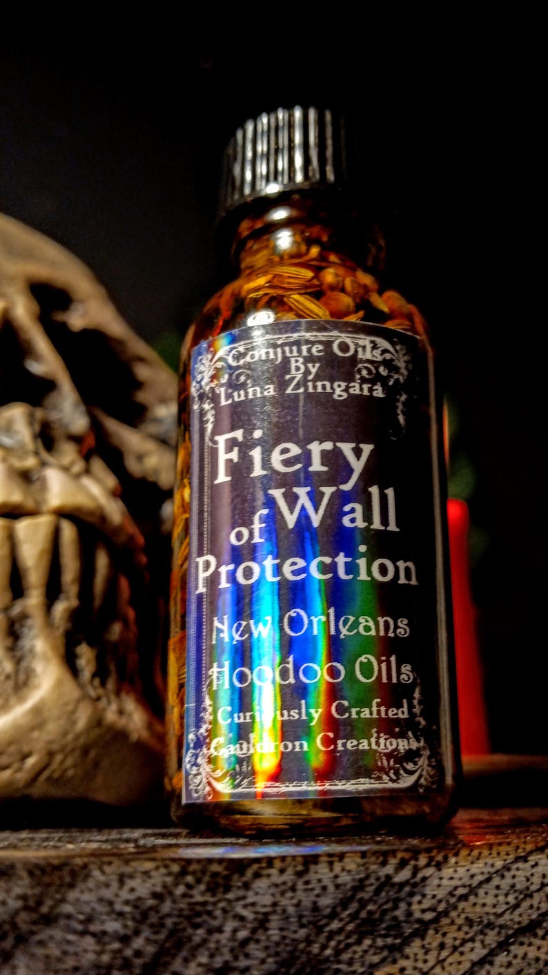 May include: A glass bottle filled with herbs and a label that reads "Conjure Oils By Luna Zingara Fiery of Wall Protection New Orleans Hoodoo Oils Curiously Crafted Cauldron Creations".