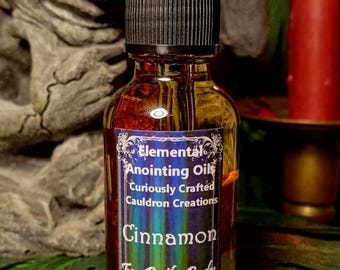 May include: A small glass bottle with a black dropper top and a label that reads "Elemental Anointing Oils Curiously Crafted Cauldron Creations Cinnamon For Bath, Body & Besom 30 Ml".