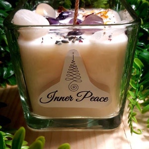 Pode incluir: Um frasco de vela quadrado de vidro com uma vela branca e um pavio de madeira. A vela &eacute; coberta com cristais e flores secas. O frasco tem um r&oacute;tulo que diz "Inner Peace".