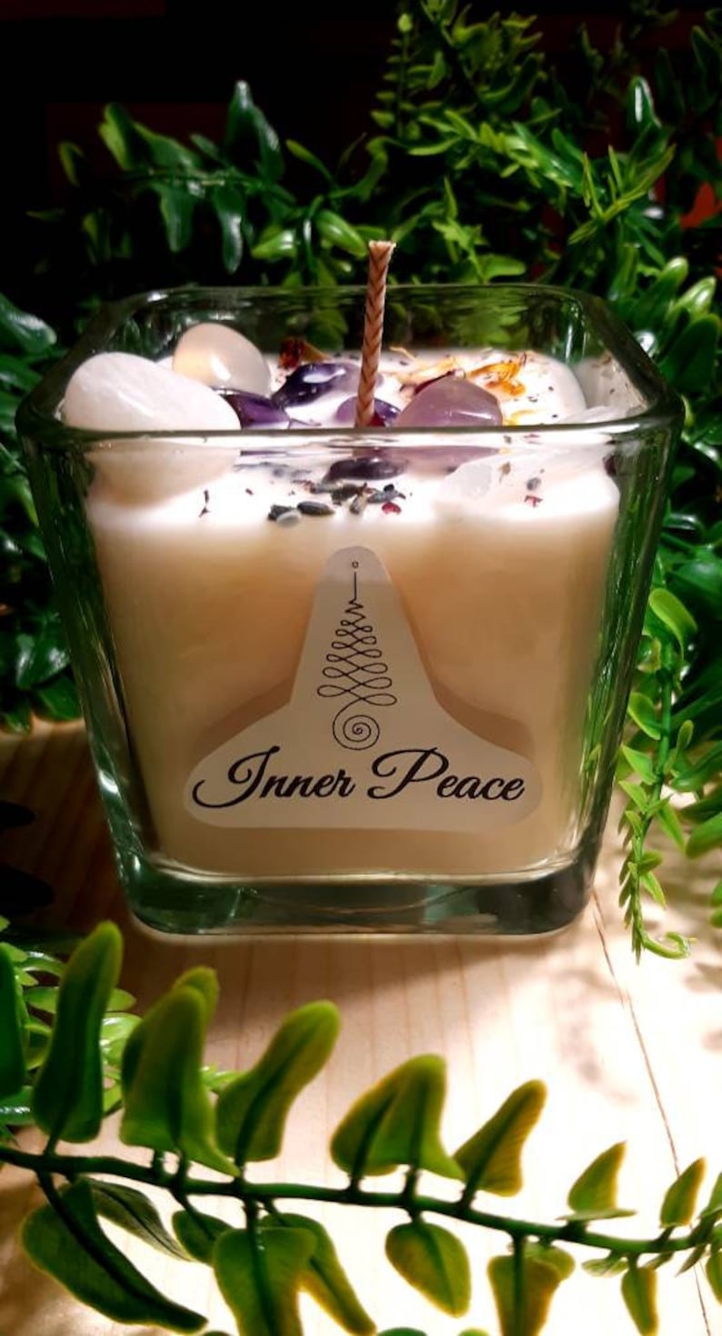 Pode incluir: Um frasco de vela quadrado de vidro com uma vela branca e um pavio de madeira. A vela &eacute; coberta com cristais e flores secas. O frasco tem um r&oacute;tulo que diz "Inner Peace".