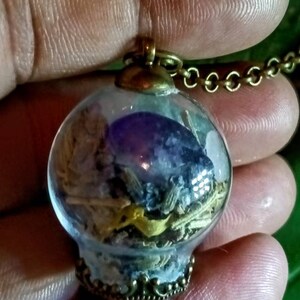 May include: A glass orb pendant necklace with a brass chain. The orb contains dried herbs, crystals, and a purple amethyst stone.