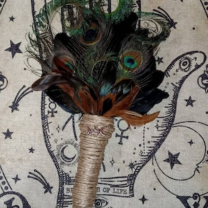 May include: A peacock feather fan with a brown leather handle and a triple moon charm. The fan is set against a background of a palmistry chart with stars and moons.