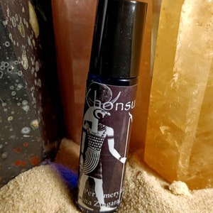 May include: A black roller bottle with a label featuring an illustration of the Egyptian god,  "Khonsu", in black and white. The label also includes the text "Perfumery" and "Luna Zagara".