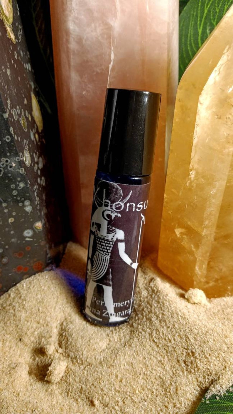 May include: A black roller bottle with a label featuring an illustration of the Egyptian god,  "Khonsu", in black and white. The label also includes the text "Perfumery" and "Luna Zagara".