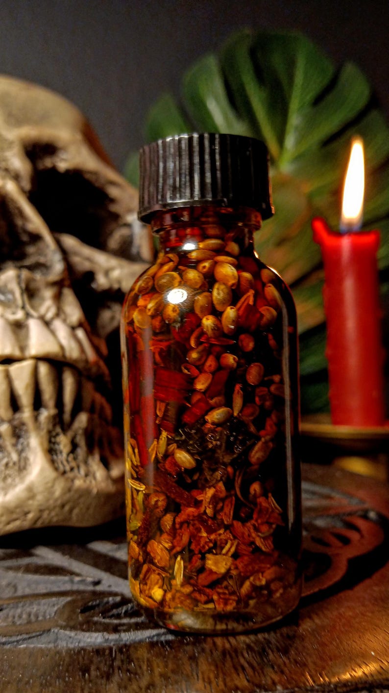 May include: A small glass bottle filled with a dark liquid and various herbs and spices. The bottle has a black screw-on cap and is sitting on a wooden surface.