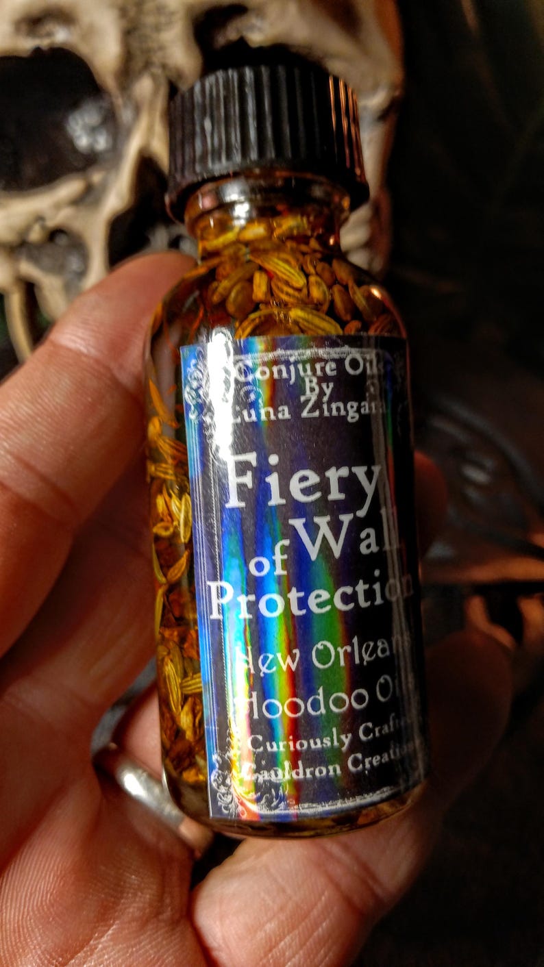 May include: A small glass bottle filled with herbs and a label that reads "Conjure Oil By Luna Zingara Fiery Wall of Protection New Orleans Hoodoo Oil Curiously Crafted Cauldron Creations".