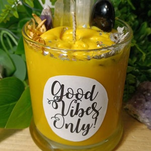 May include: A yellow candle in a glass jar with a white label that says "Good Vibes Only!" The candle is surrounded by crystals and dried herbs.