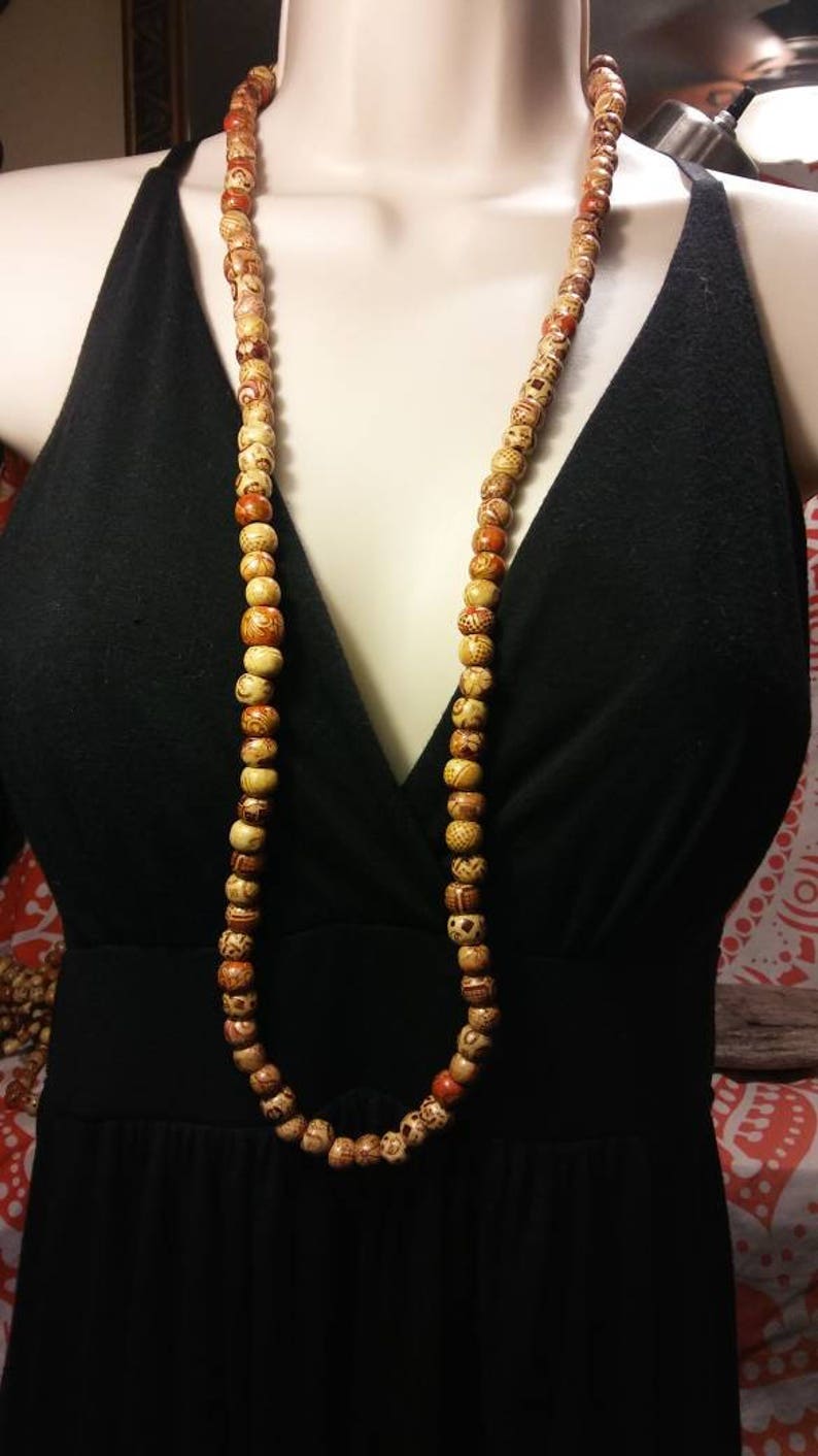 May include: A long necklace made of wooden beads with intricate patterns. The beads are a mix of light brown and orange colors.