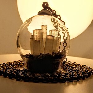 Peut inclure: Un collier avec un pendentif en forme de globe en verre et une cha&icirc;ne dor&eacute;e. &Agrave; l'int&eacute;rieur du globe se trouvent des cristaux de s&eacute;l&eacute;nite blancs.