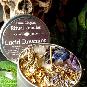 May include: A silver tin candle with a black label that reads "Luna Zingara Ritual Candles Lucid Dreaming". The candle is filled with white wax, dried herbs, and crystals.