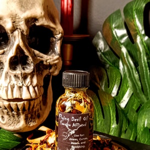 May include: A small glass bottle filled with a golden liquid and herbs. The bottle has a black label with the text "Flying Devil Oil For the Afflicted" and instructions for use. The label also includes the text "Luna Zingara's Curiously Crafted Cauldron Creations".
