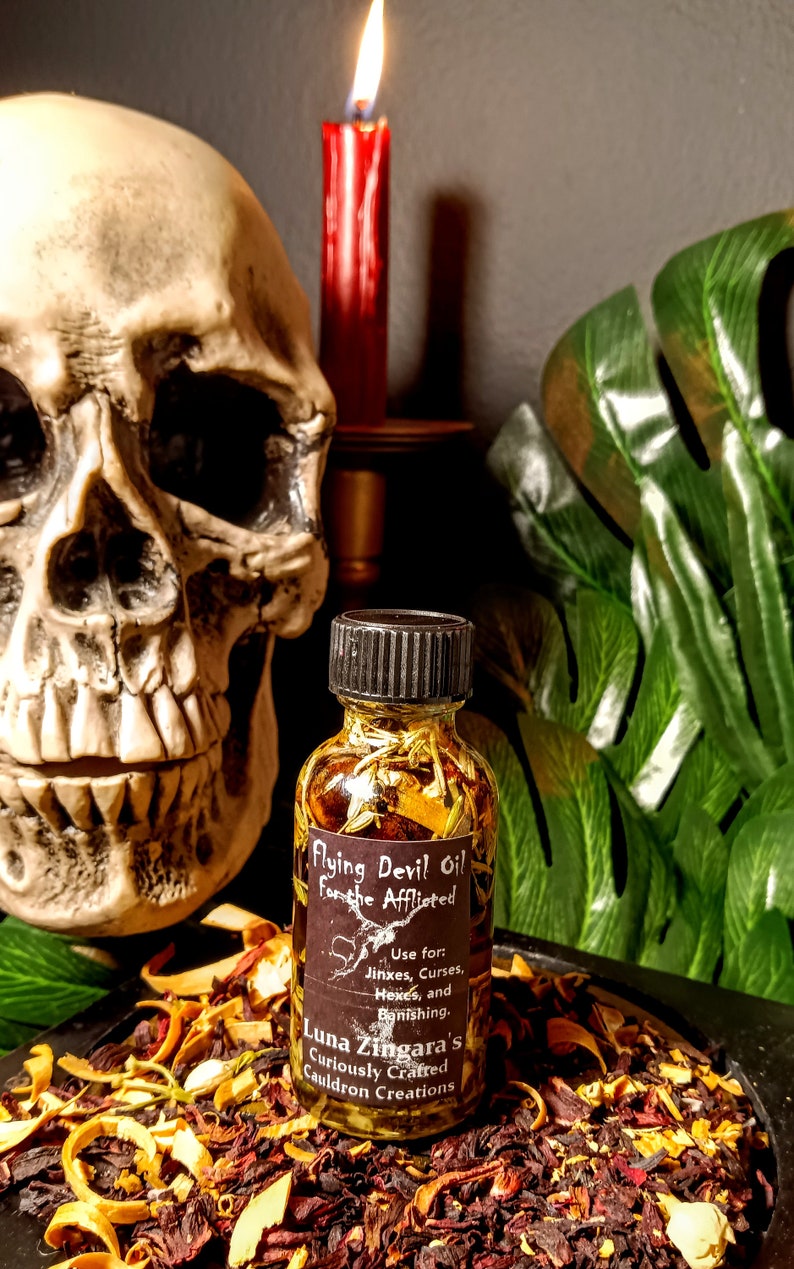 May include: A small glass bottle filled with a golden liquid and herbs. The bottle has a black label with the text "Flying Devil Oil For the Afflicted" and instructions for use. The label also includes the text "Luna Zingara's Curiously Crafted Cauldron Creations".