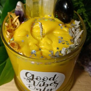 May include: Yellow candle in a glass jar with a white label that says "Good Vibes Only". The candle is decorated with crystals, dried flowers, and glitter.