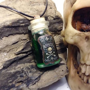May include: A green glass bottle pendant necklace with a cork stopper and a black leather cord. The bottle has a label that reads "POISON" with a skull and crossbones.