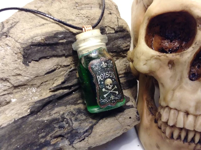 May include: A green glass bottle pendant necklace with a cork stopper and a black leather cord. The bottle has a label that reads "POISON" with a skull and crossbones.
