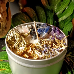 May include: A silver candle tin with a white candle and various crystals and herbs. The crystals include amethyst, clear quartz, black obsidian, and blue sodalite. The herbs include lavender, sage, and dried grasses.
