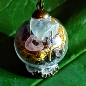 May include: A glass orb necklace with a brass chain and a variety of crystals and dried flowers inside. The orb is clear and the crystals are pink, blue, and purple.