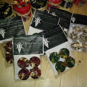 K&ouml;nnte beinhalten: Vier Pakete Teelichtkerzen mit verschiedenen Kr&auml;utern und Kristallen. Die Pakete sind mit "Gypsy Moon Candle Company" und "Come Here Boy" beschriftet.