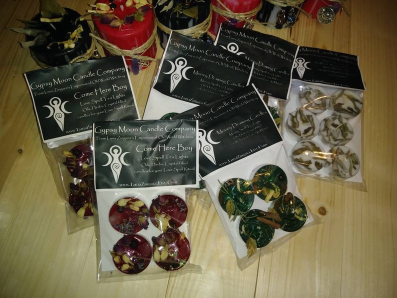 K&ouml;nnte beinhalten: Vier Pakete Teelichtkerzen mit verschiedenen Kr&auml;utern und Kristallen. Die Pakete sind mit "Gypsy Moon Candle Company" und "Come Here Boy" beschriftet.