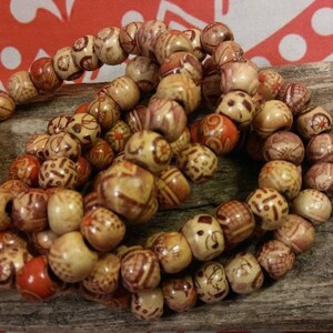 May include: A close-up of a set of wooden bead bracelets. The beads are a light brown color with intricate patterns carved into them. Some of the beads have a reddish-brown color.