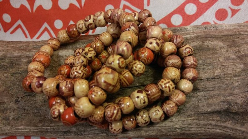 May include: A close-up of a set of wooden bead bracelets. The beads are a light brown color with intricate patterns carved into them. Some of the beads have a reddish-brown color.