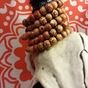 May include: A stack of wooden bead bracelets with red, orange, and brown accents. The bracelets are on top of a white skull with black eyes.
