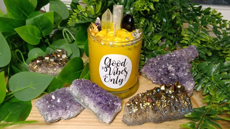 May include: A yellow candle with a label that reads "Good Vibes Only!" surrounded by amethyst and gold crystals.
