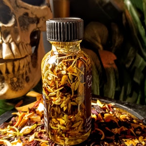 May include: A small glass bottle with a black lid filled with a yellow liquid and herbs. The bottle is sitting on a bed of dried flowers and herbs.