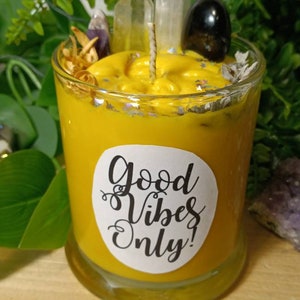 May include: Yellow candle with a white label that says "Good Vibes Only!" The candle is in a glass jar and has crystals and other decorative elements on top.