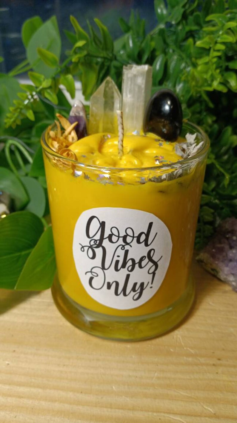 May include: Yellow candle with a white label that says "Good Vibes Only!" The candle is in a glass jar and has crystals and other decorative elements on top.