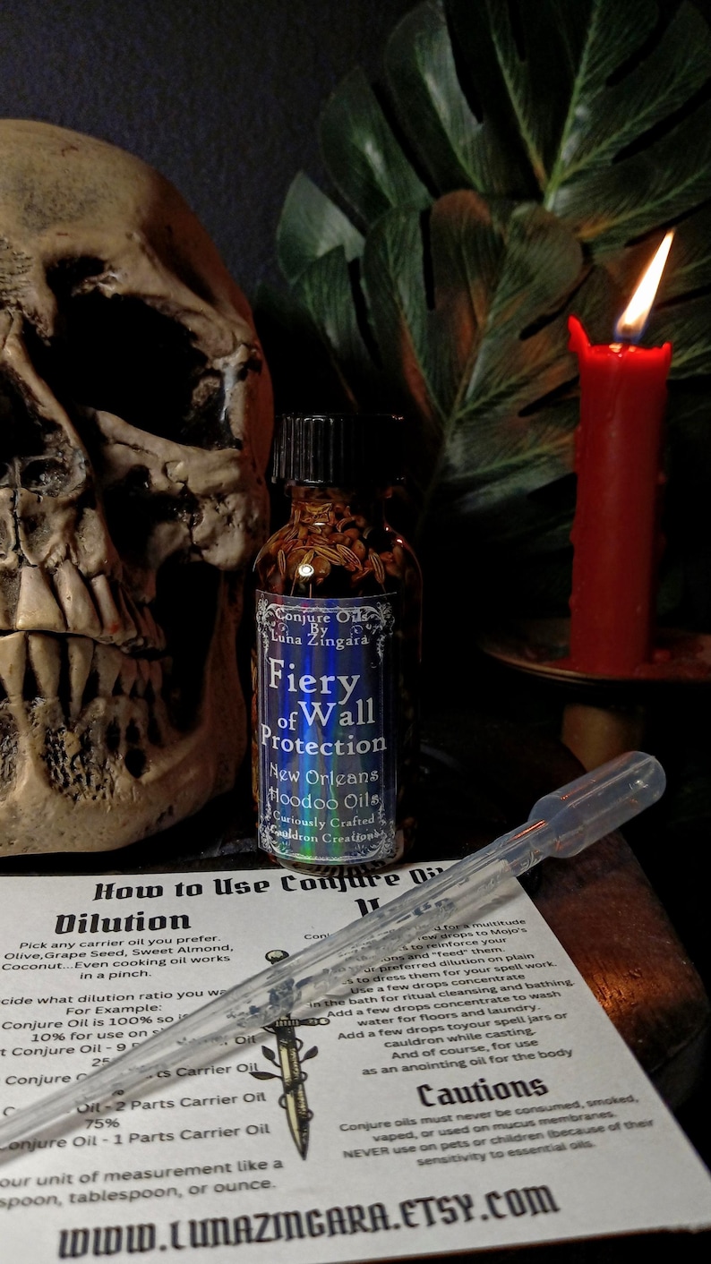 May include: A small glass bottle with a dark brown cap filled with a clear liquid and herbs. The bottle label reads "Conjure Oil by Luna Zingara Fiery Wall Protection New Orleans Hoodoo Oils Curiously Crafted Cauldron Creations". The bottle is sitting on a white card with instructions on how to use the oil, including dilution ratios. The card also includes a warning about the oil's use.