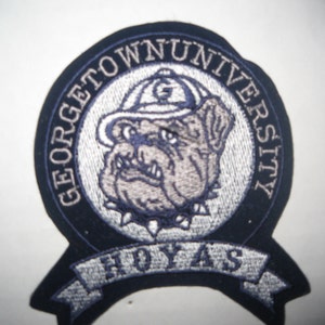 Puede incluir: Parche bordado con el logotipo de la Universidad de Georgetown. El parche azul marino tiene texto blanco que dice "GEORGETOWN UNIVERSITY". Un bulldog con sombrero está en el centro, con "HOYAS" en la parte inferior.
