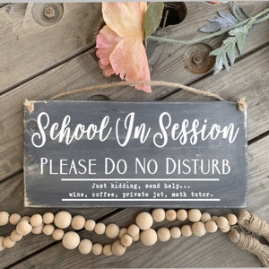 May include: A black wooden sign with white text that reads "School In Session PLEASE DO NO DISTURB Just kidding, send help... wine, coffee, private jet, math tutor."