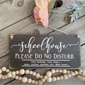 May include: A black wooden sign with white text that reads "Schoolhouse Please Do No Disturb" and "Just kidding, send help... wine, coffee, private jet, math tutor."