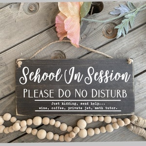 May include: A black wooden sign with white text that reads "School In Session PLEASE DO NO DISTURB Just kidding, send help... wine, coffee, private jet, math tutor."