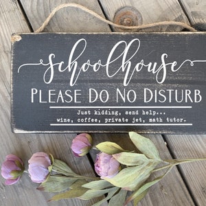 May include: Black wooden sign with white text that reads "Schoolhouse Please Do No Disturb" and "Just kidding, send help... wine, coffee, private jet, math tutor."