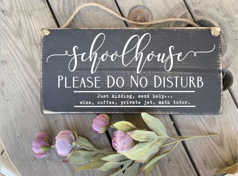 May include: Black wooden sign with white text that reads "Schoolhouse Please Do No Disturb" and "Just kidding, send help... wine, coffee, private jet, math tutor."