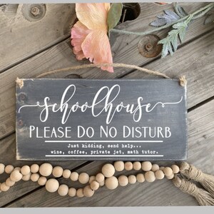 May include: A black wooden sign with white text that reads "Schoolhouse Please Do No Disturb" and "Just kidding, send help... wine, coffee, private jet, math tutor."