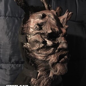 May include: A detailed, brown Hemlock mask with a textured, wood-like appearance. The mask features prominent, branch-like protrusions and is secured with a black strap. The word "HEMLOCK" is displayed in white text at the bottom.